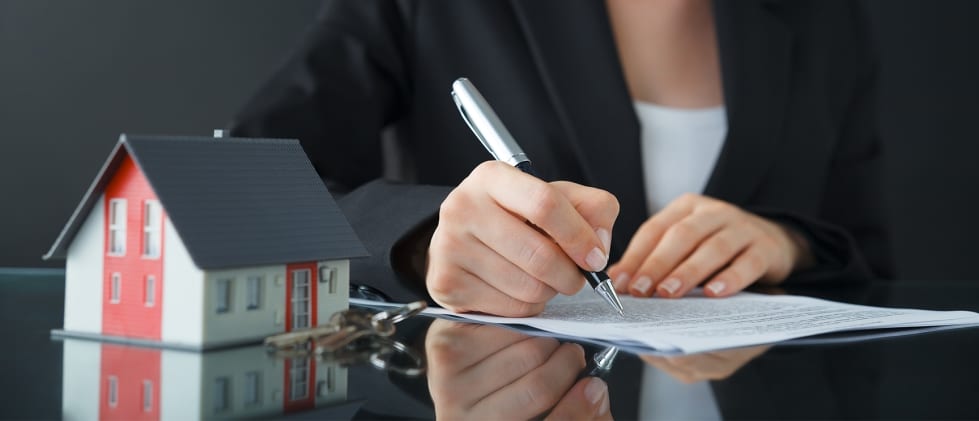 Model of a house with keys next to a person signing a contract
